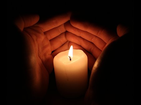 Image of two hands warming around a candle.